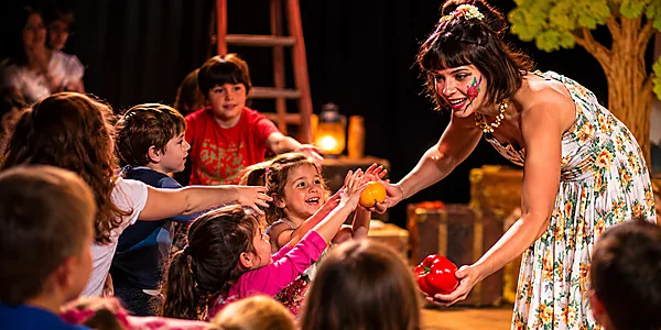 Conteuse présentant des fruits et légumes à des enfants lors d'un spectacle de contes éducatifs et participatifs.